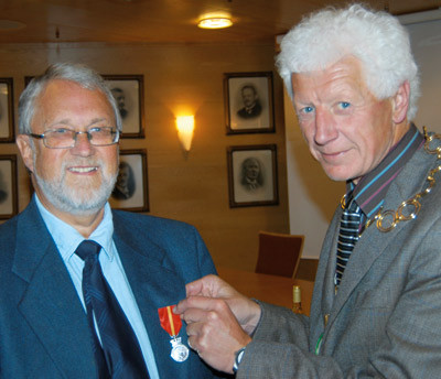 Overlege Per E. M. Bjerke mottar H.M. Kongens fortjenstmedalje i s&oslash;lv av ordf&oslash;rer i Hamar Einar Busterud. Foto Trond Tend&oslash;&hellip;