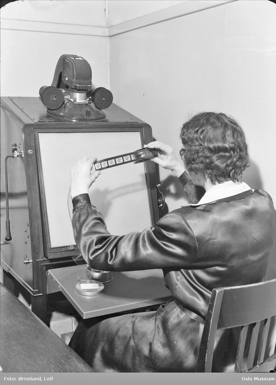 Avlesning av mikrofilm, fotografert i 1953 i Riksarkivet den gang det l&aring; p&aring; Bankplassen 3, der Arkitekturmuseet n&aring; holder&hellip;